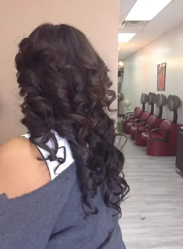 Woman with long curly dark hair in a salon, shown from behind near styling chairs.