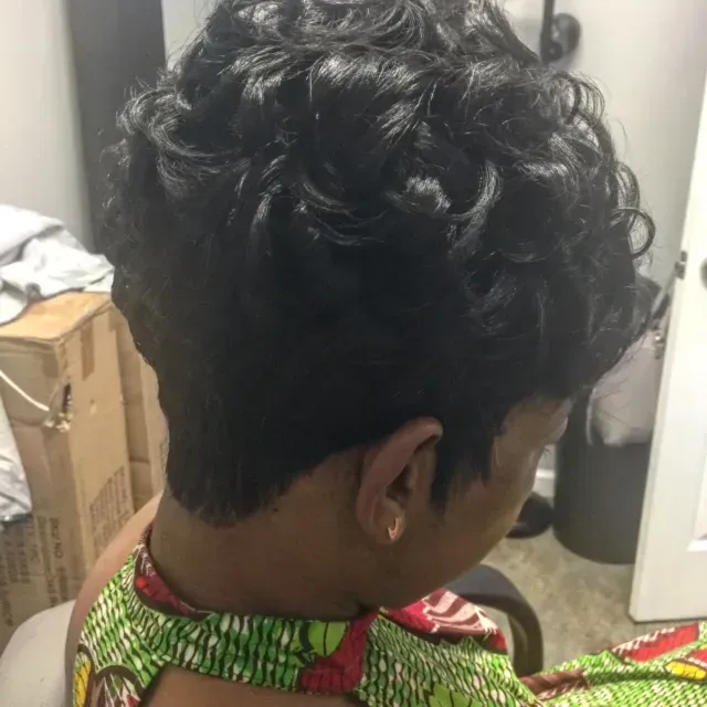 Person with short sides and curly hair, seen from behind indoors, wearing a green patterned shirt.