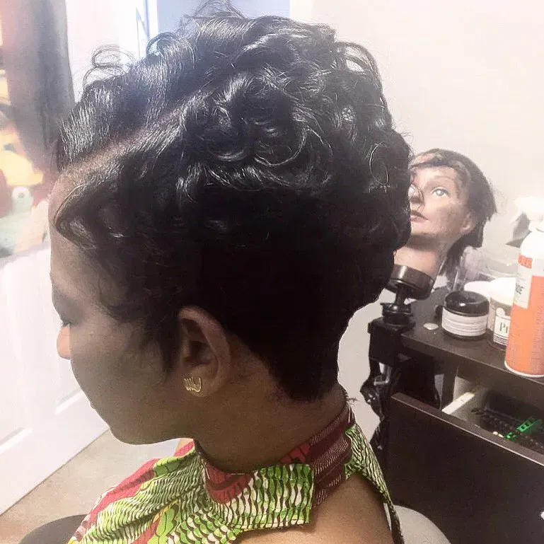 Woman with an updo hairstyle in a salon, wearing a green and red patterned cape; mannequin head in background