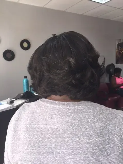 Person seated in an office, seen from behind, with short dark hair and a gray shirt.