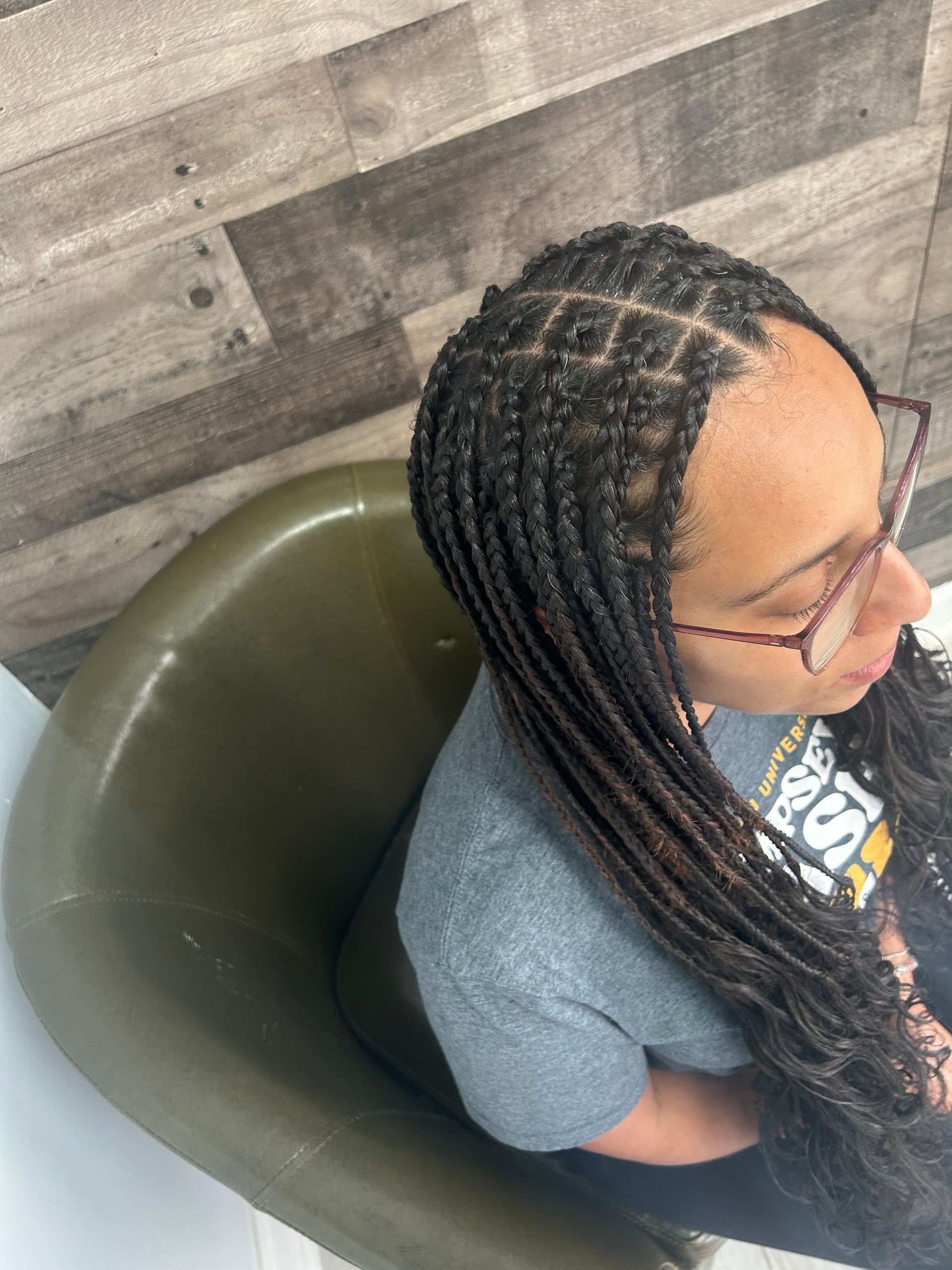 Top-down view of a person with braids seated in a green chair against a wood-paneled wall.