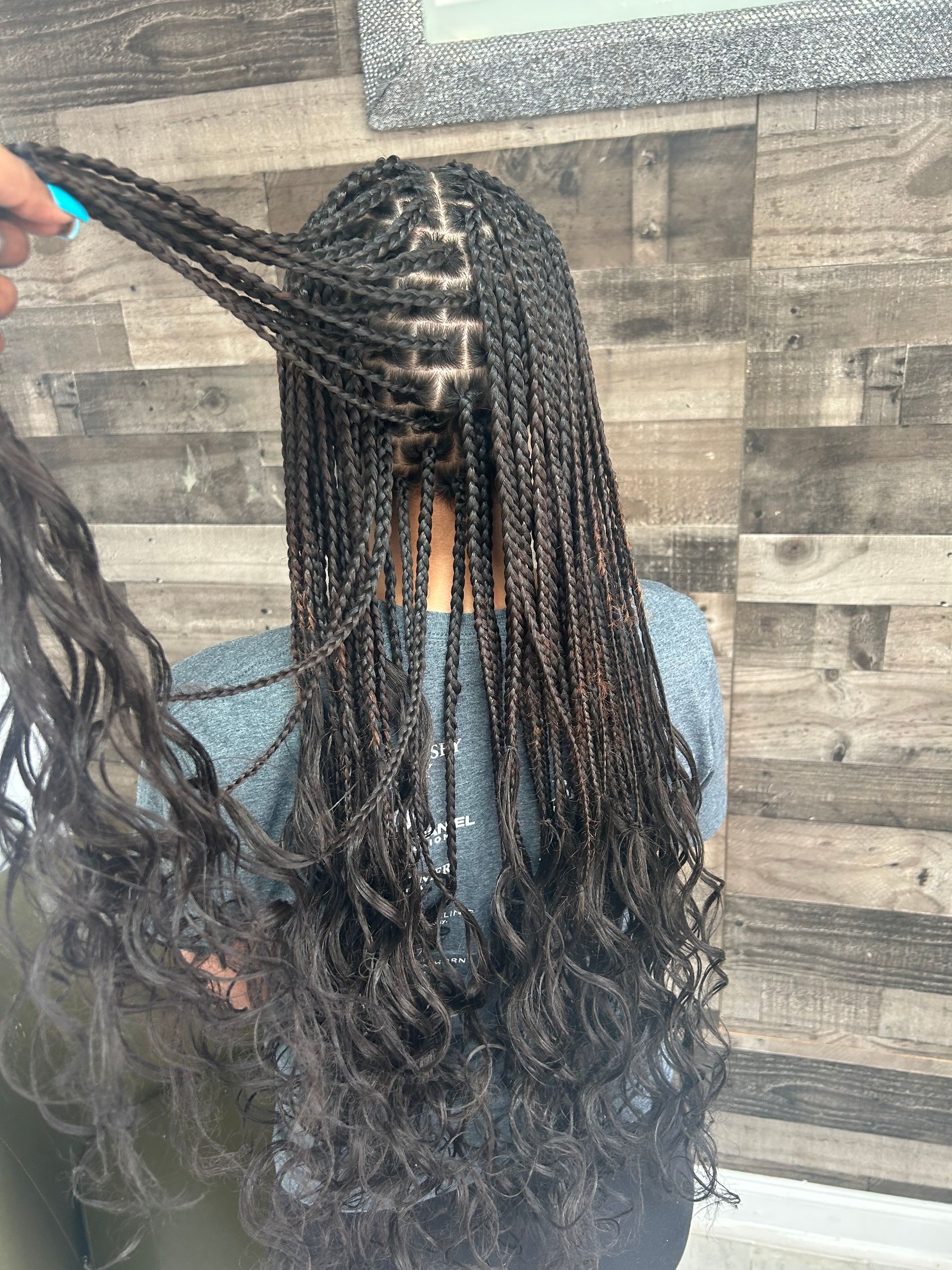 Person with long black braided hair being styled against a wood-paneled wall