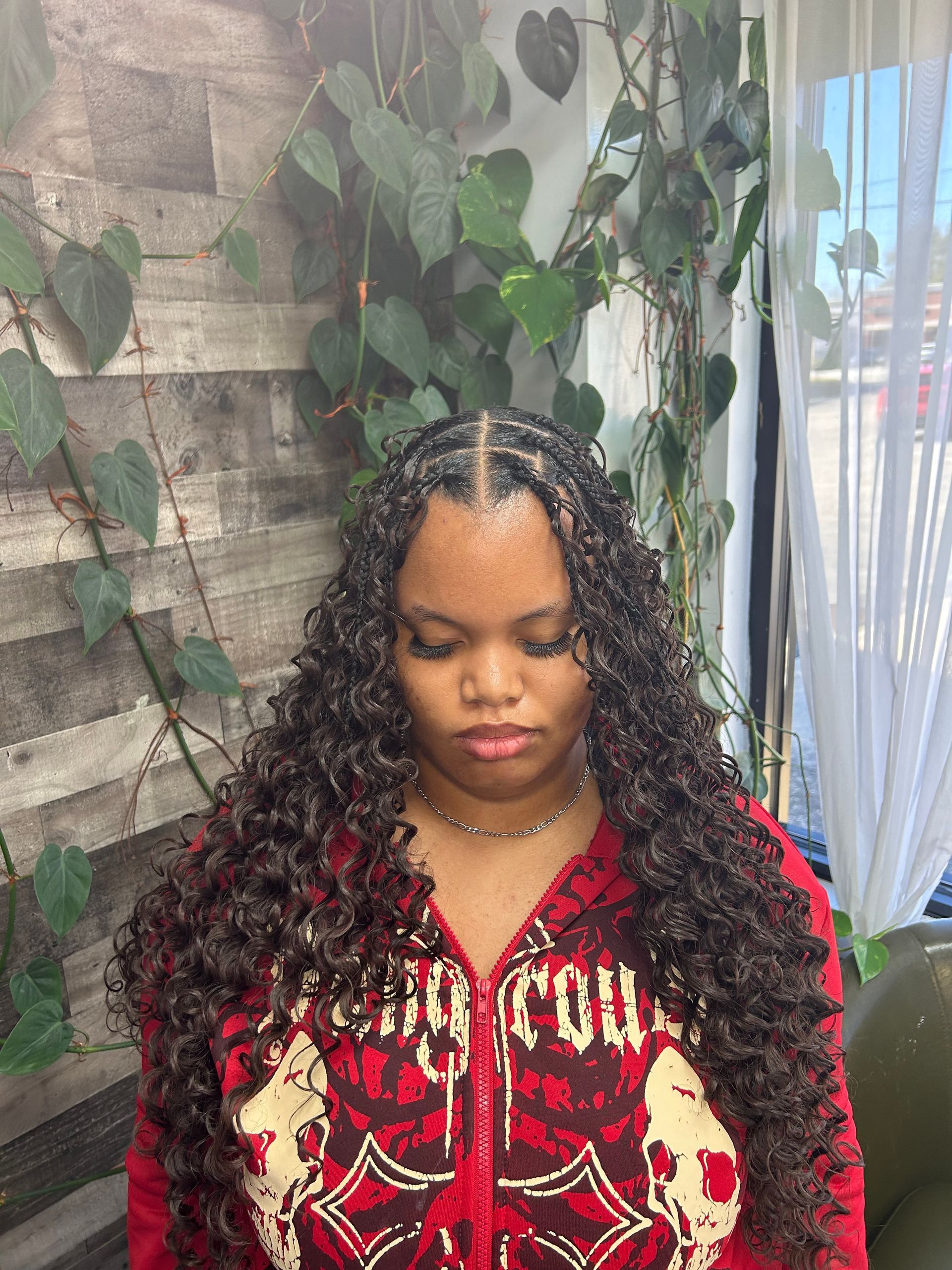 Person in a red patterned top standing before a brick wall and greenery, looking down.