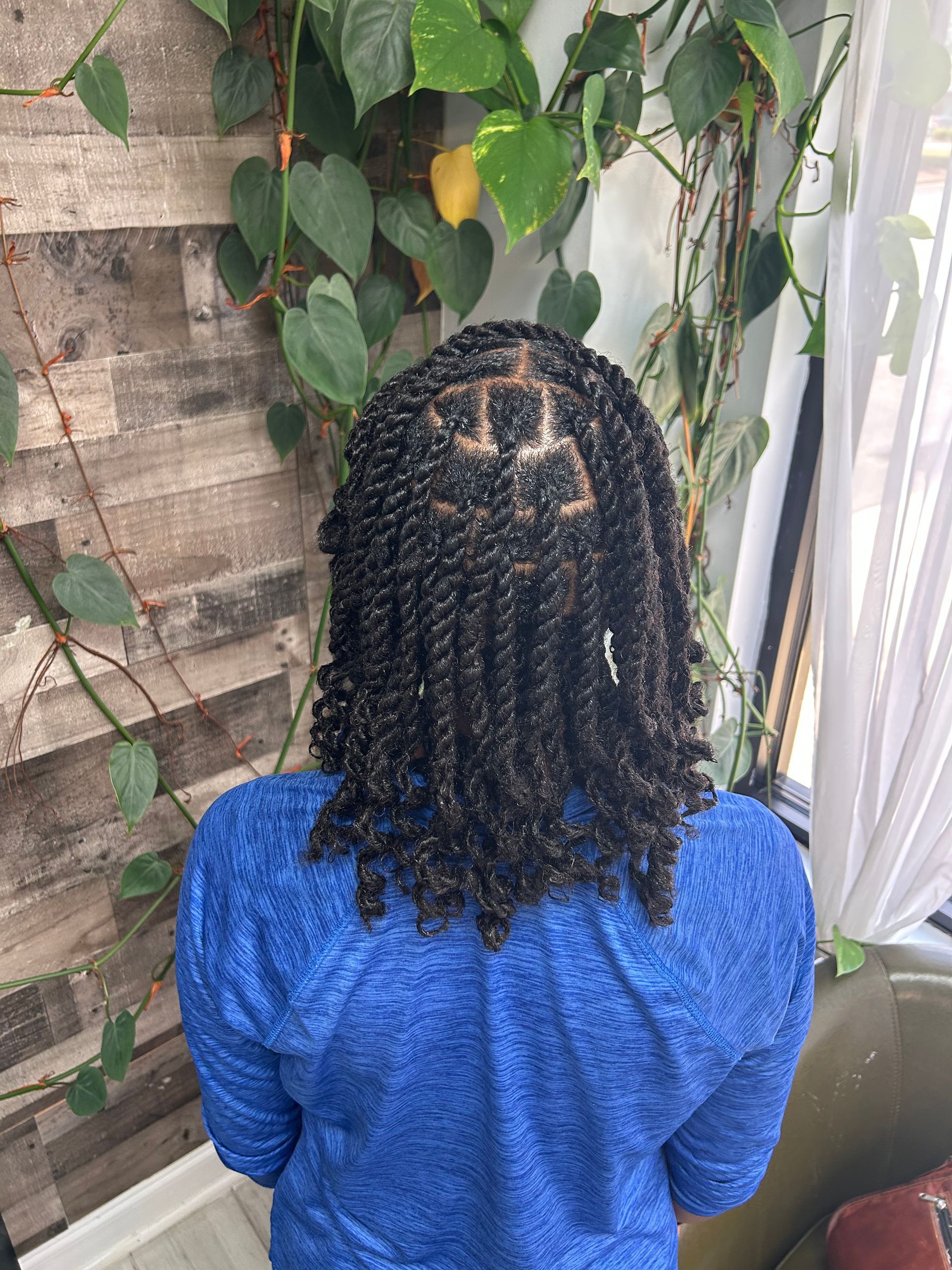 Person with braided hair in a blue top seen from behind, standing near a vine-covered wall.