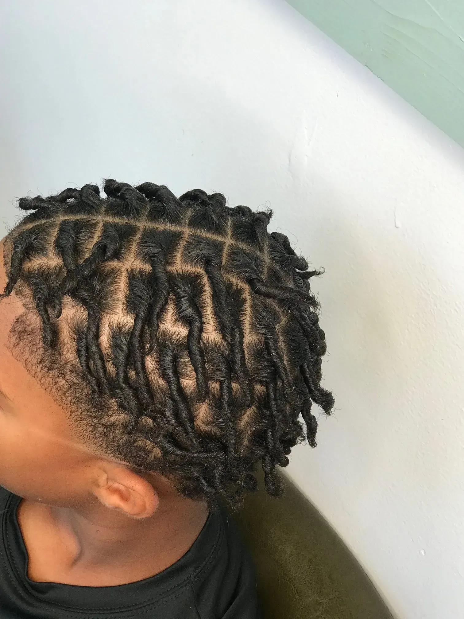 Profile view of short twisted braids with shaved sides against a light wall