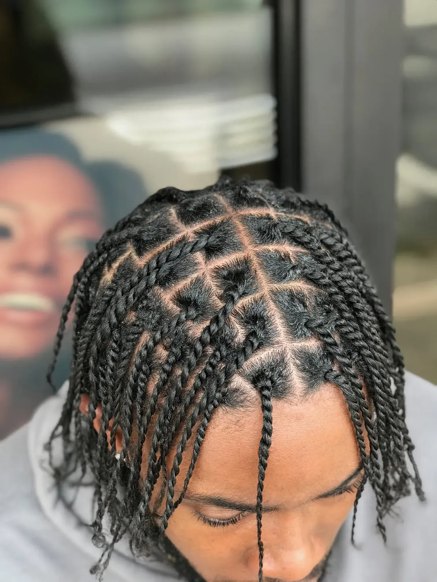 Close-up of braided hair with a parted scalp pattern, head tilted down indoors.