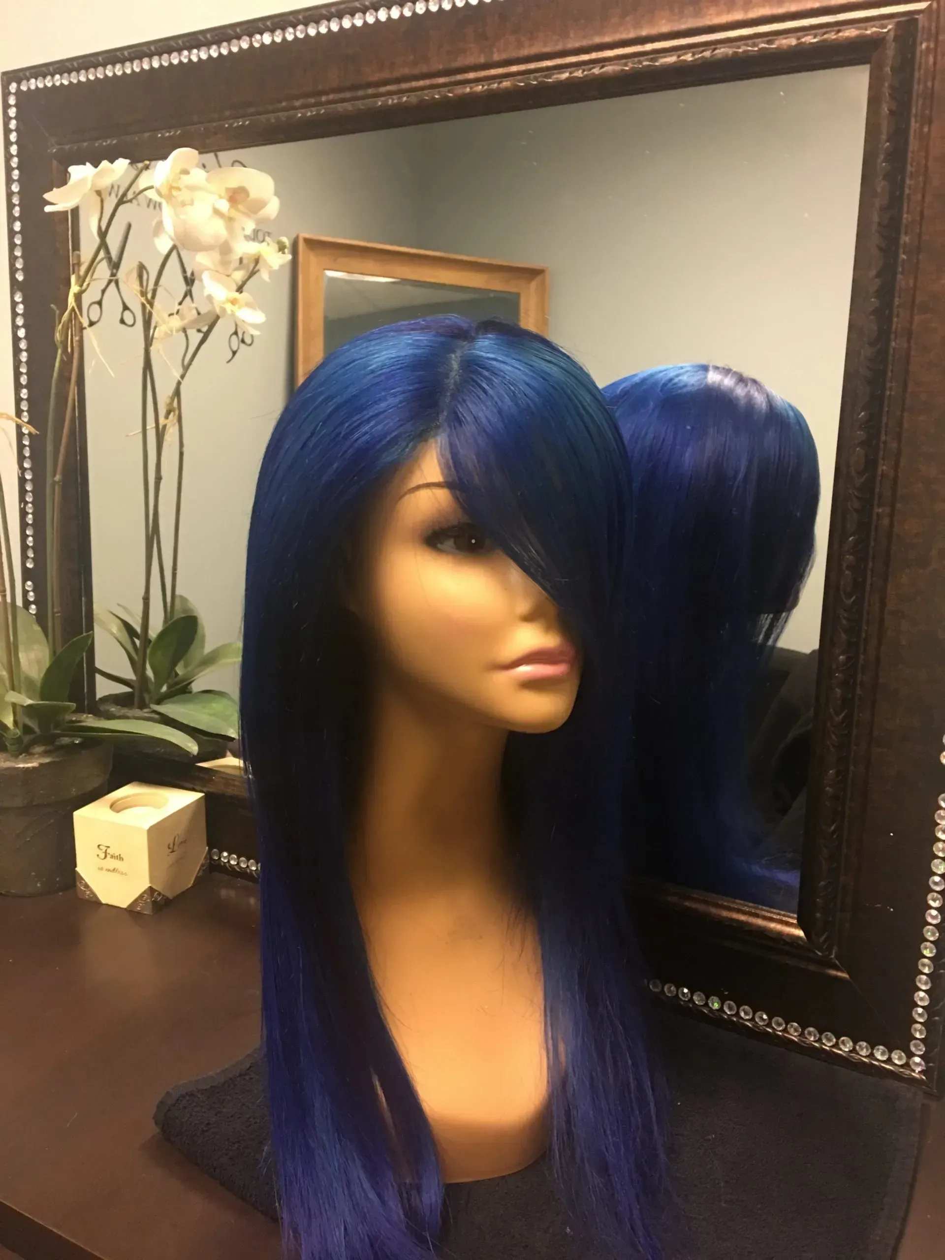 Blue wig on a mannequin head beside a mirror, with a white orchid in the background.