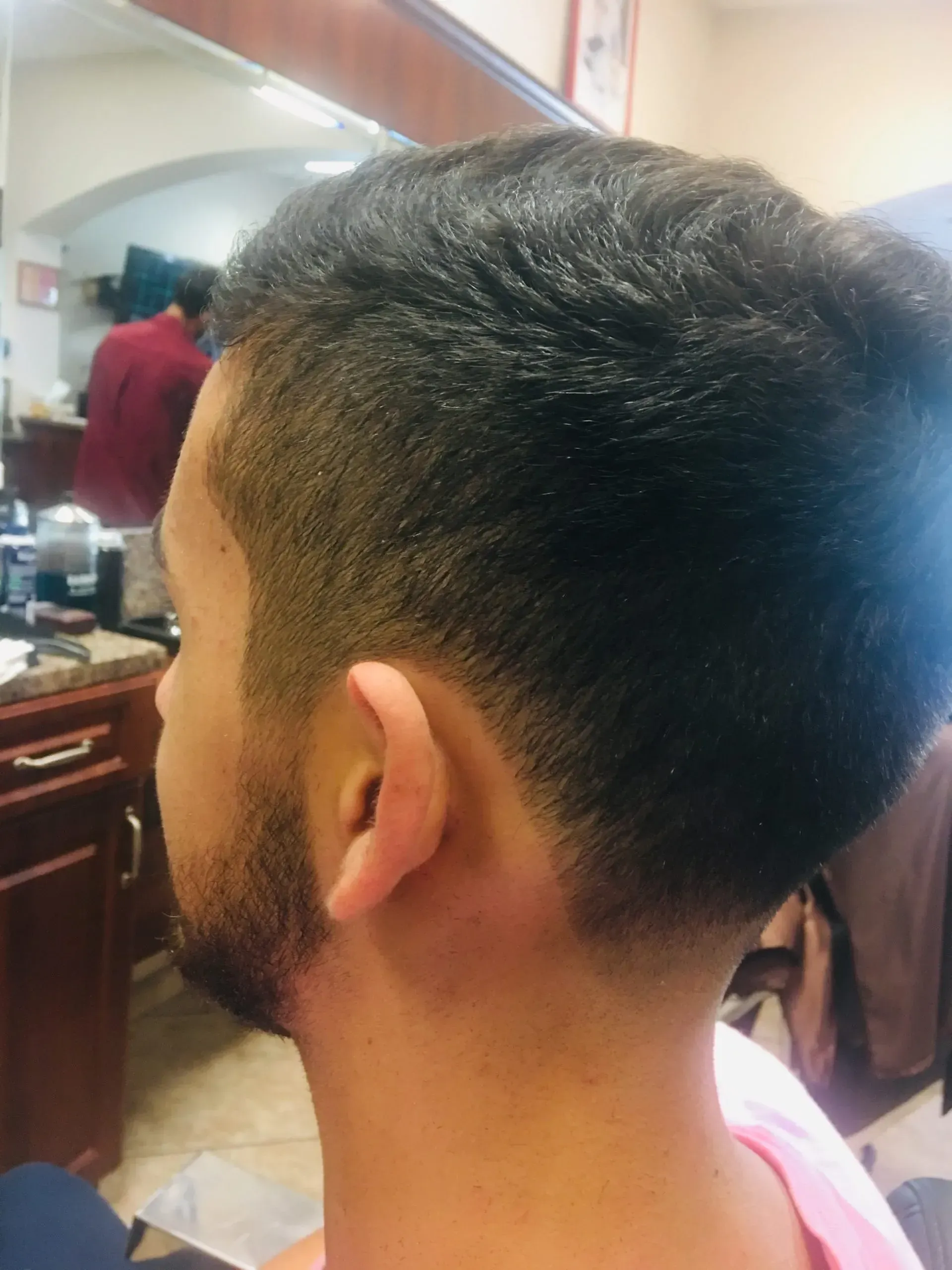 Side view of a short-haired person sitting in a barber shop, with a faded haircut and trimmed beard.
