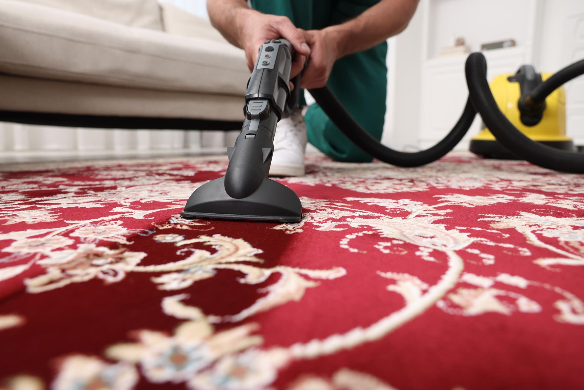 A man is cleaning a red rug with a vacuum cleaner.