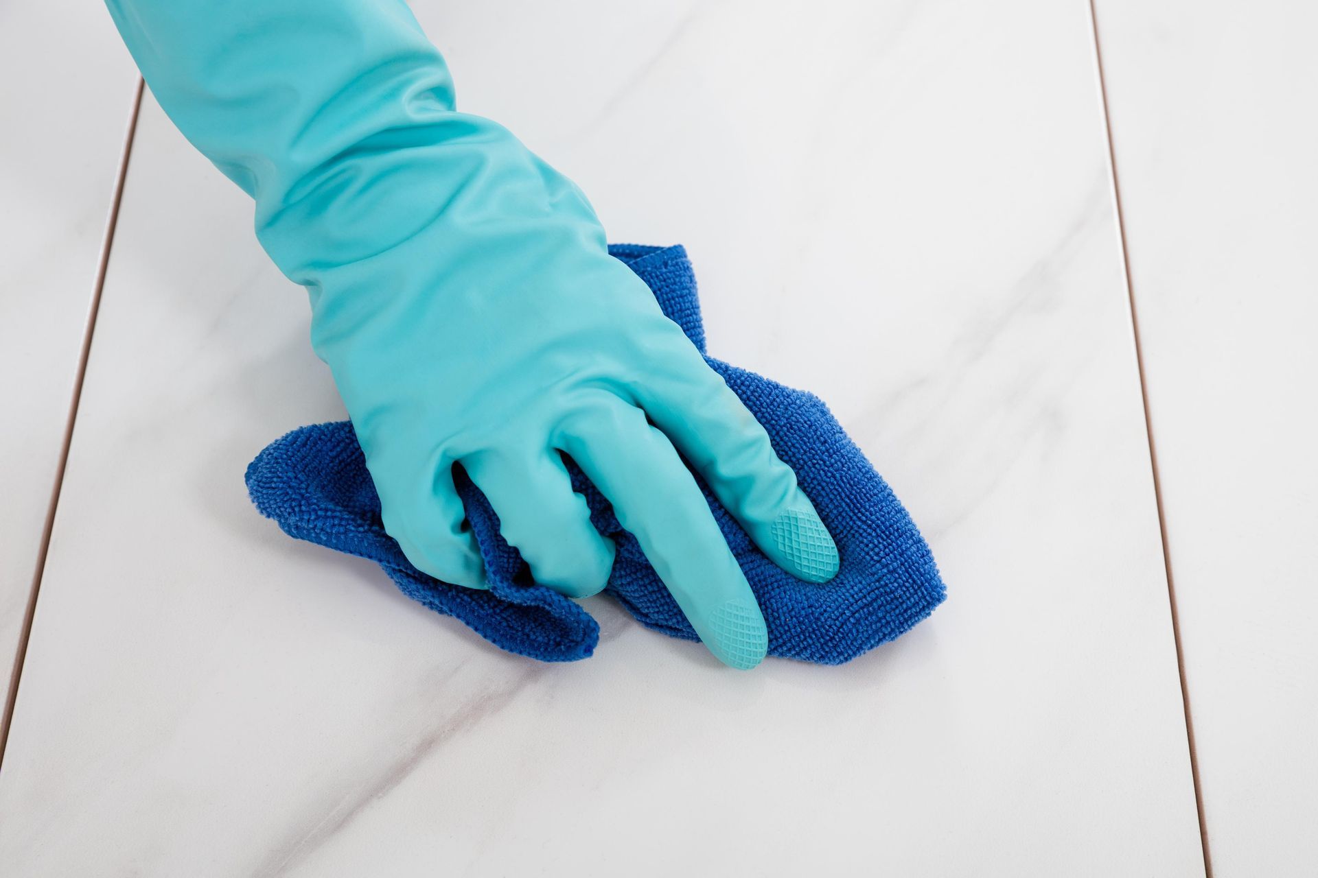 A person wearing blue gloves is cleaning a tile floor with a blue cloth.