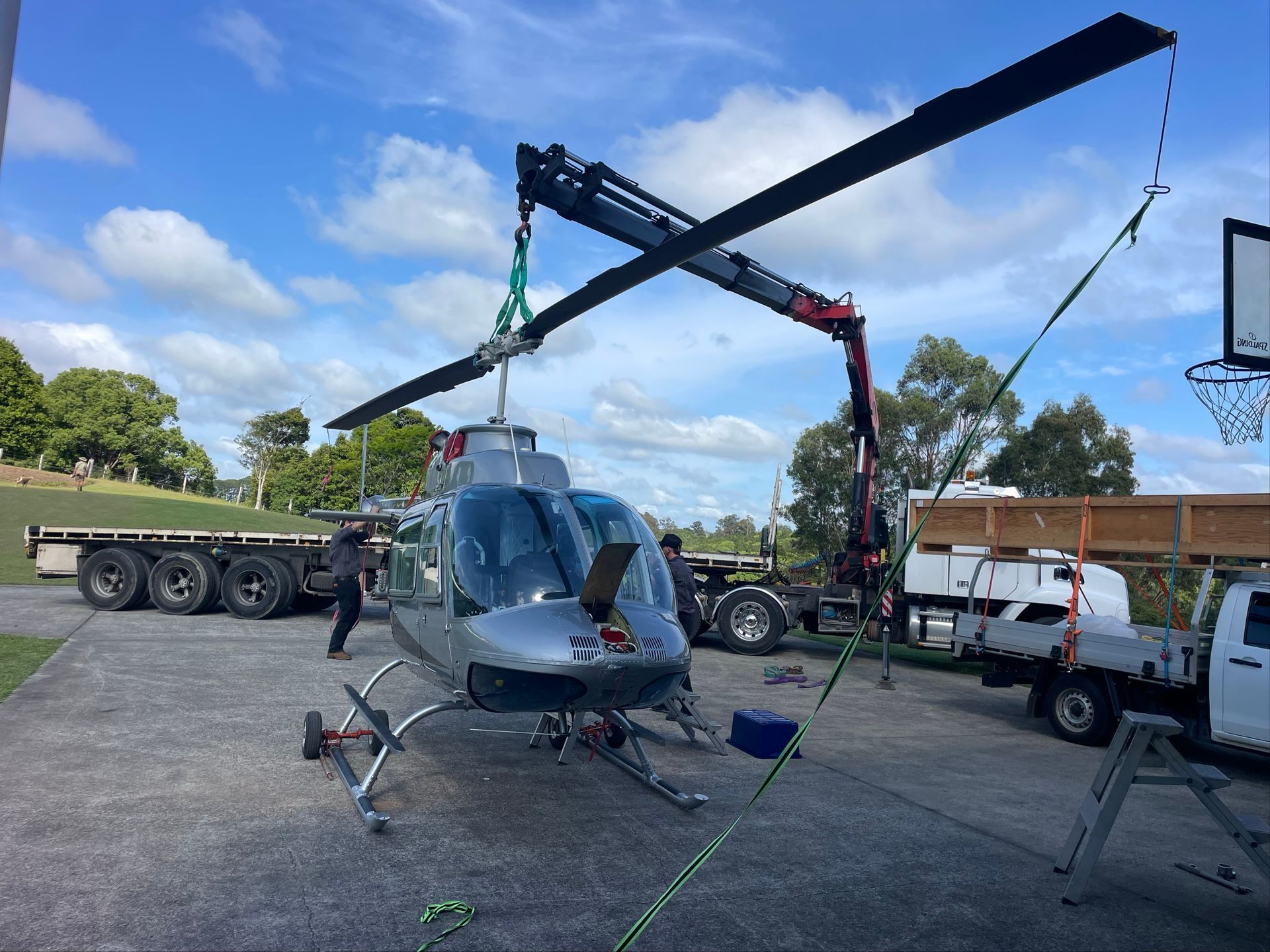 Helicopter being lifted by a crane in a gravel lot, with trucks and a trailer nearby. — Trucking Crane Trucks in Caboolture, QLD