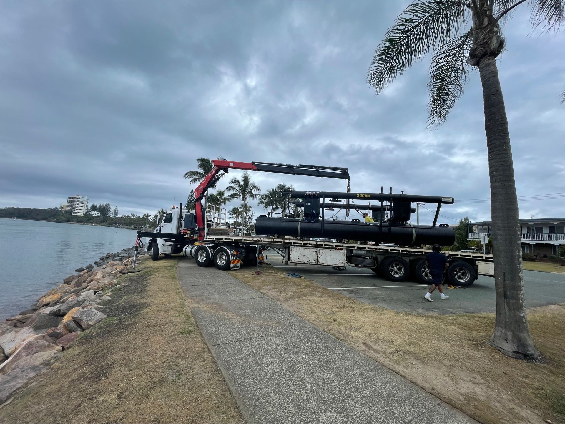 Boat being lifted by a crane on a trailer near a waterfront dock on a cloudy day — Trucking Crane Trucks in Caboolture, QLD