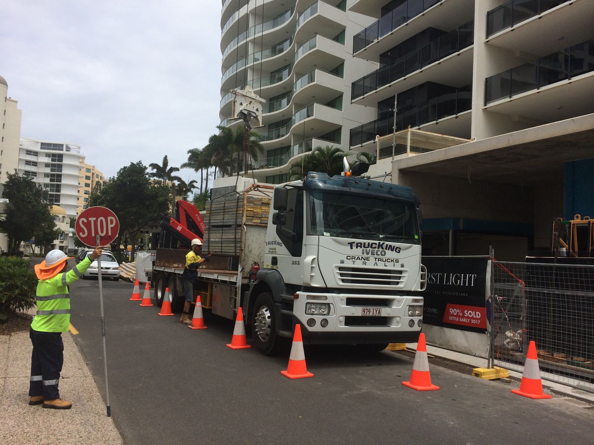 Traffic worker directing a white truck through orange cones on a city street beside apartments — Trucking Crane Trucks in Warana, QLD