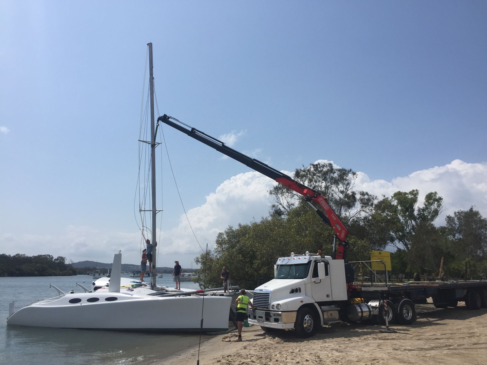 Crane truck loading a white sailboat on a trailer at a waterfront dock — Trucking Crane Trucks in Caboolture, QLD