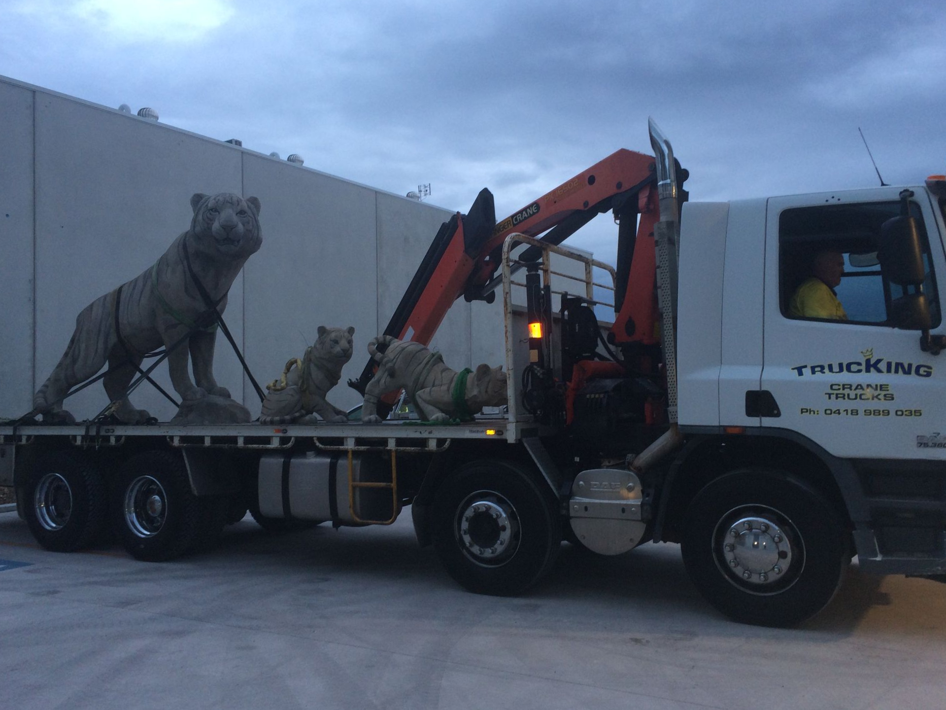 Tow truck carrying a wolf statue and a folded red crane on a flatbed trailer outdoors — Trucking Crane Trucks in Warana, QLD