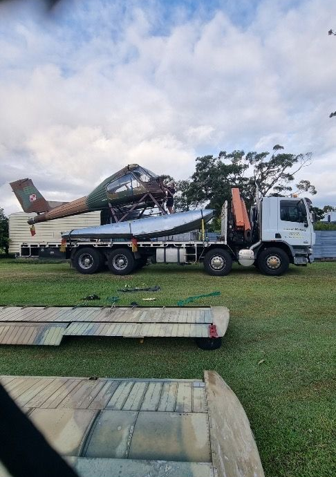 Cargo plane fuselage loaded on a flatbed truck in a grassy field, with ramps in the foreground. — Trucking Crane Trucks in Caboolture, QLD