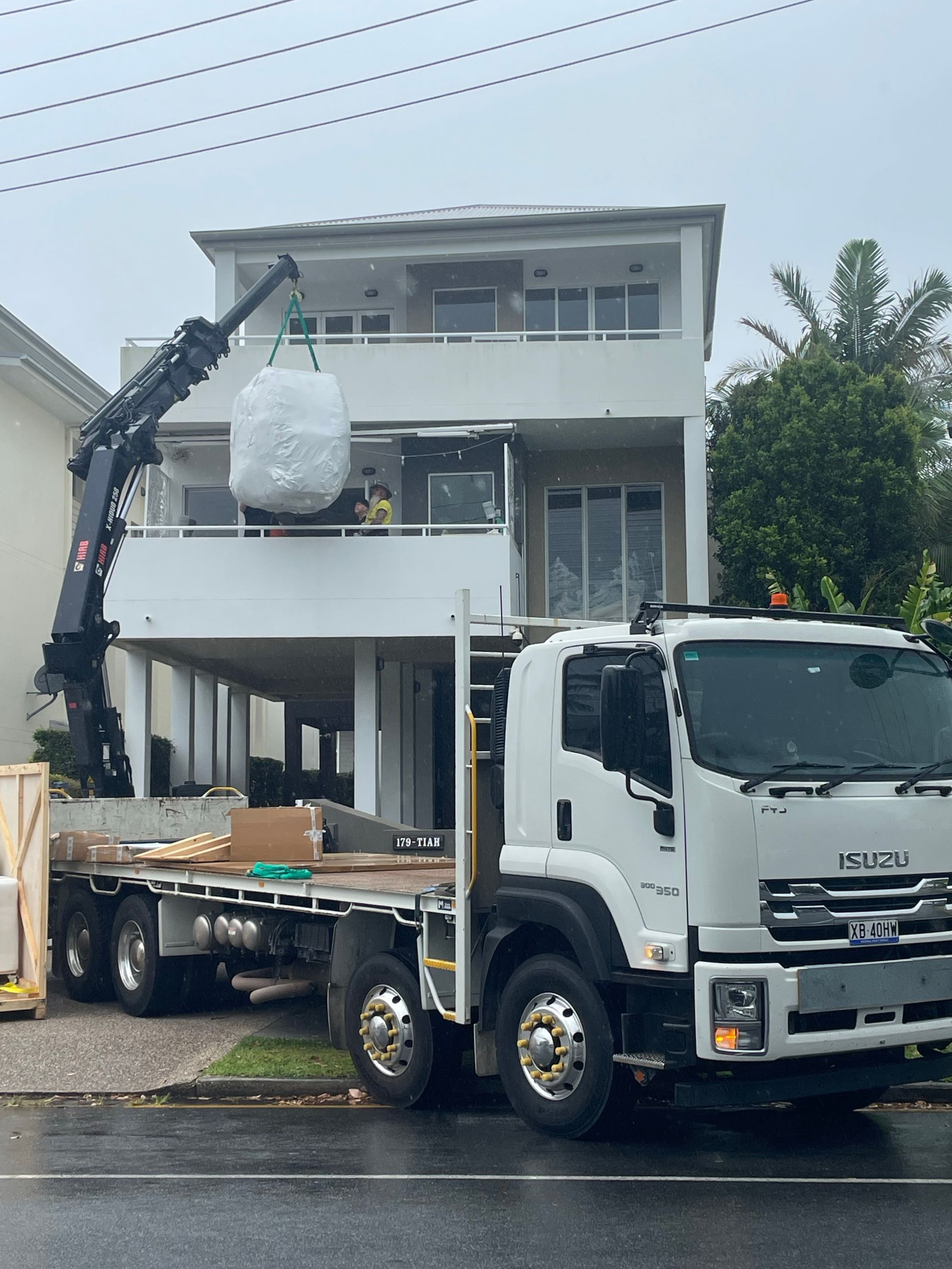 Crane truck lifting a white modular structure onto a flatbed in front of a house — Trucking Crane Trucks in Caboolture, QLD