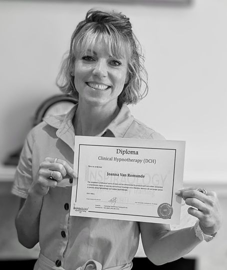 Woman in light-colored shirt smiles, holding a certificate, indoors.