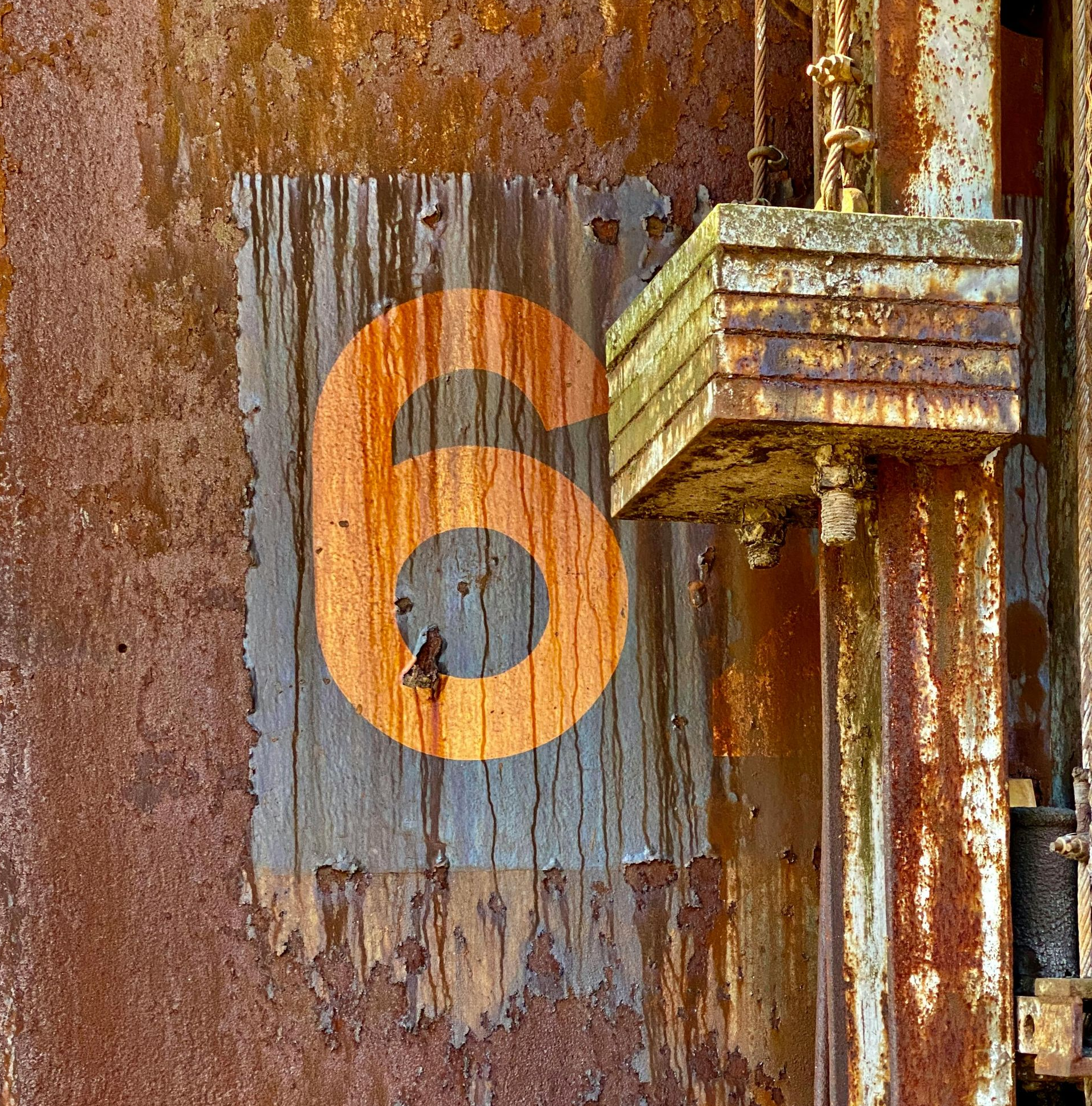 Rusty metal with an orange number 6 painted on it.