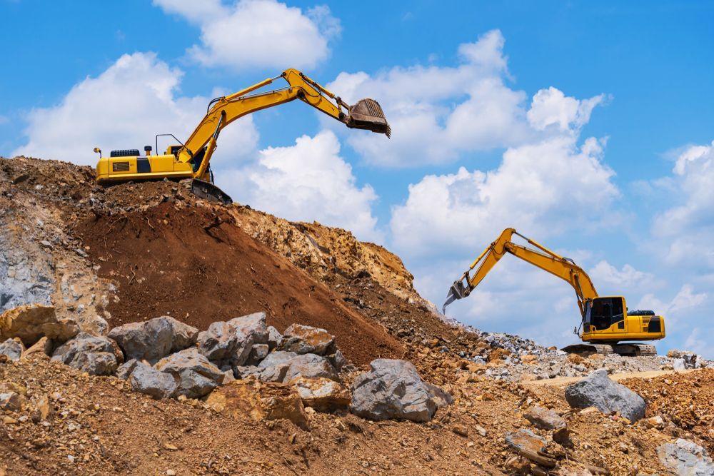 Two Yellow Excavators Working on a Rocky Dirt Hillside Under a Blue Sky — Mike Barlow Earthmoving Pty Ltd in Rockhampton, QLD