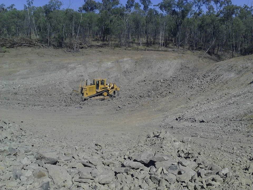 A Bulldozer Is Driving Through A Dirt Field With Trees In The Background — Mike Barlow Earthmoving Pty Ltd in Rockhampton, QLD
