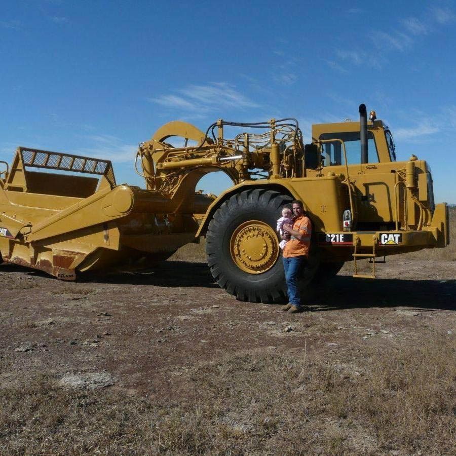 A Man Holding A Baby Stands In Front Of A Bulldozer — Mike Barlow Earthmoving Pty Ltd in Rockhampton, QLD