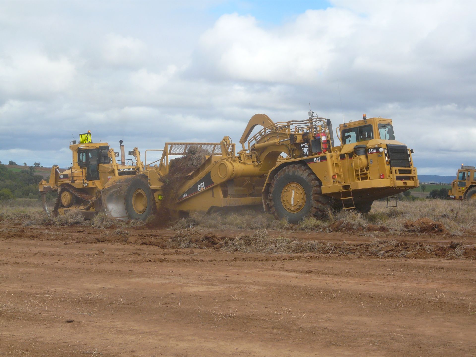 A Yellow and Black Construction Vehicle Is Parked on Top of A Dirt Field — Mike Barlow Earthmoving Pty Ltd in Gladstone, QLD