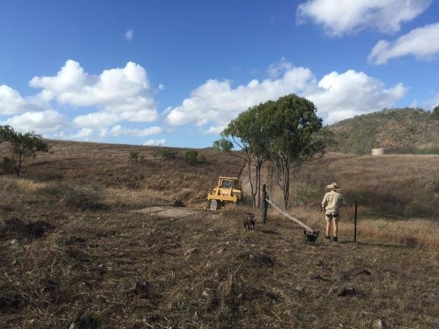 A Man Stands in a Field With a Bulldozer, Constructing a Road in the Background — Mike Barlow Earthmoving Pty Ltd in Rockhampton, QLD