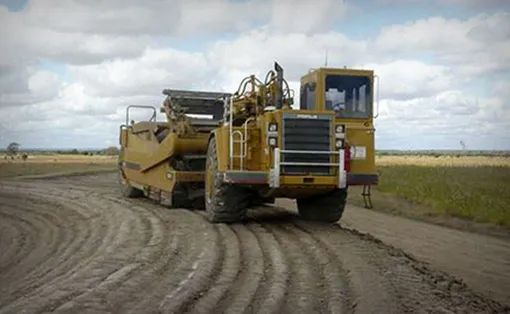 A Large Yellow Truck Is Driving Down A Dirt Road — Mike Barlow Earthmoving Pty Ltd in Rockhampton, QLD