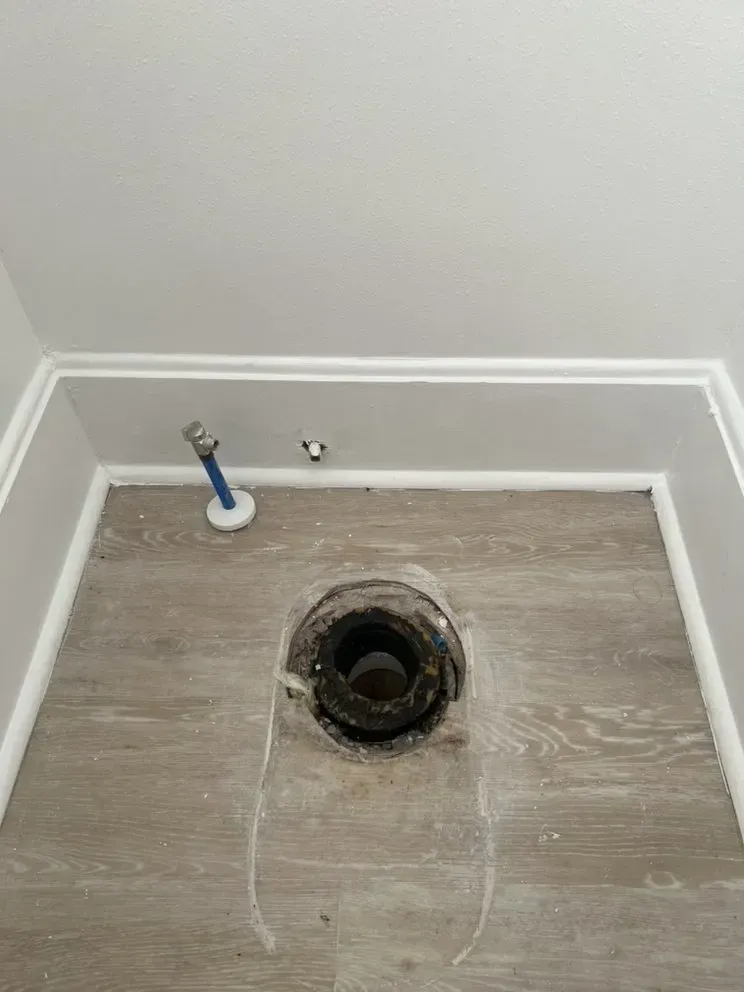 A hole in the floor of a bathroom next to a toilet.