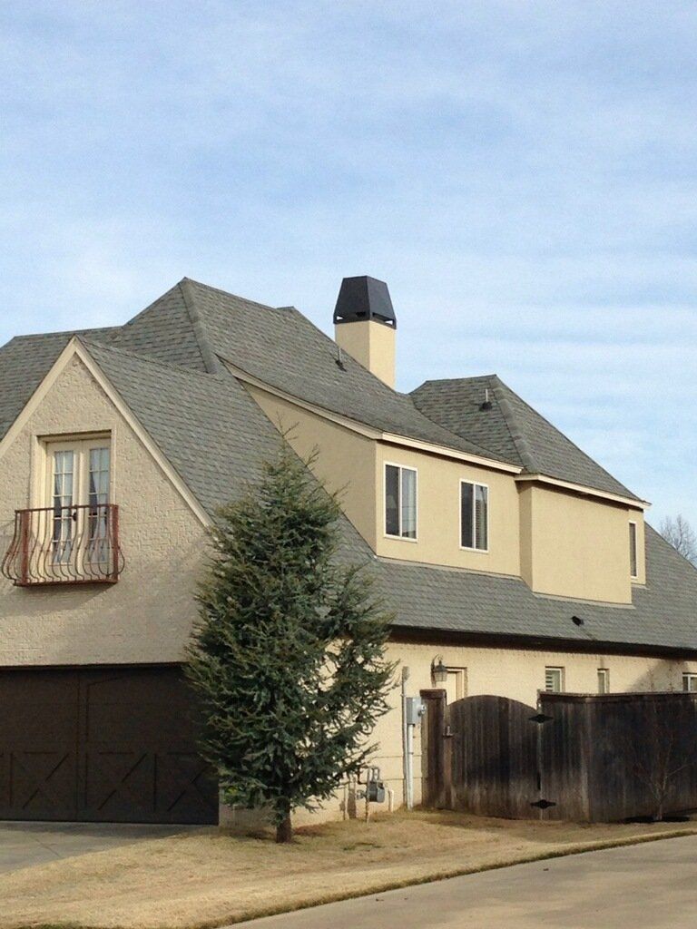 Beige two-story house with gray roof, small balcony, garage, and a tree in the front yard.