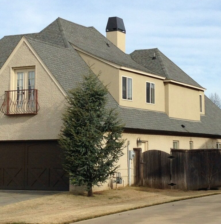 Suburban house with beige siding, gray roof, chimney, garage, and a tree in front