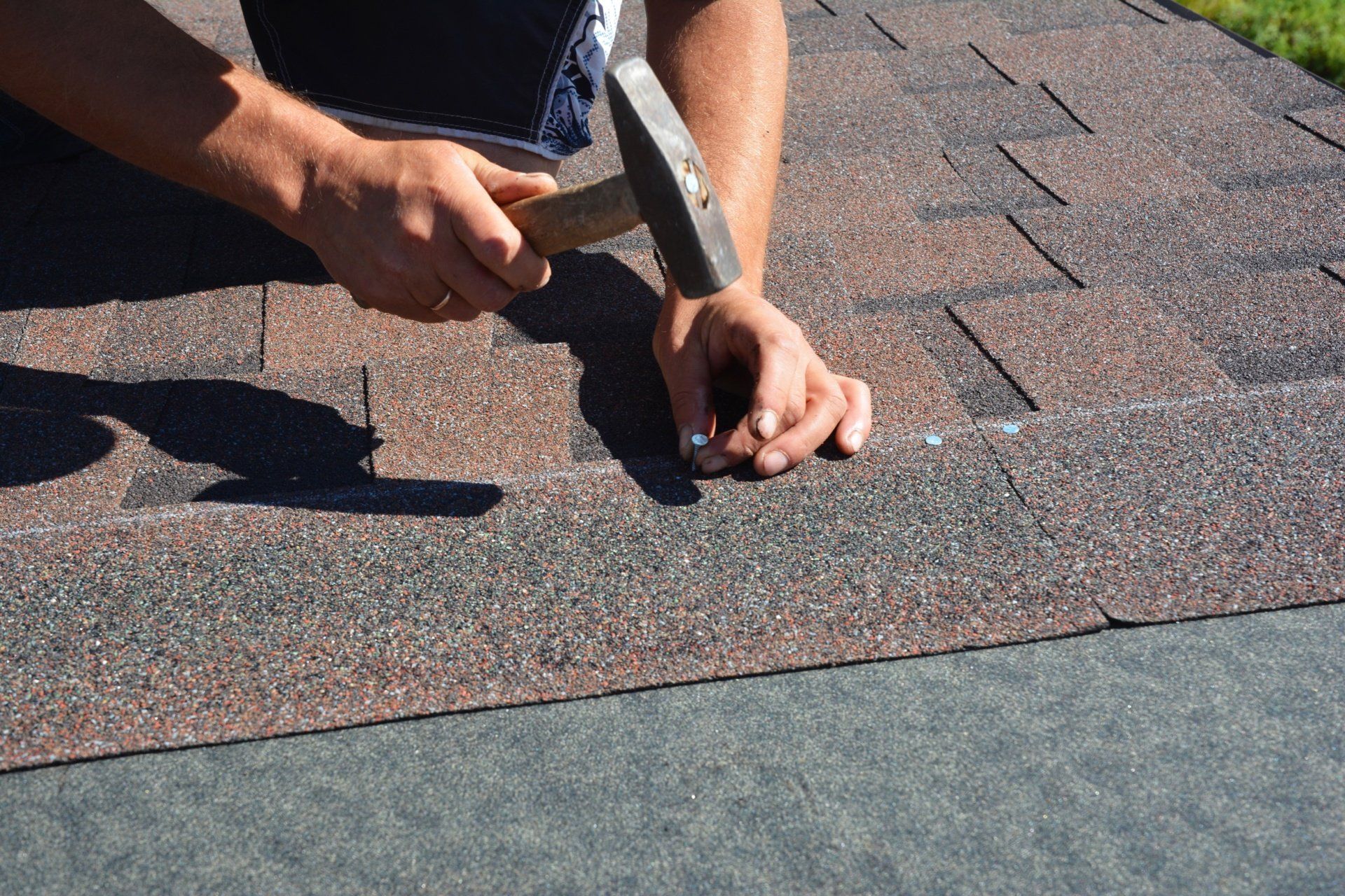 Hands hammering roofing shingles on a roof