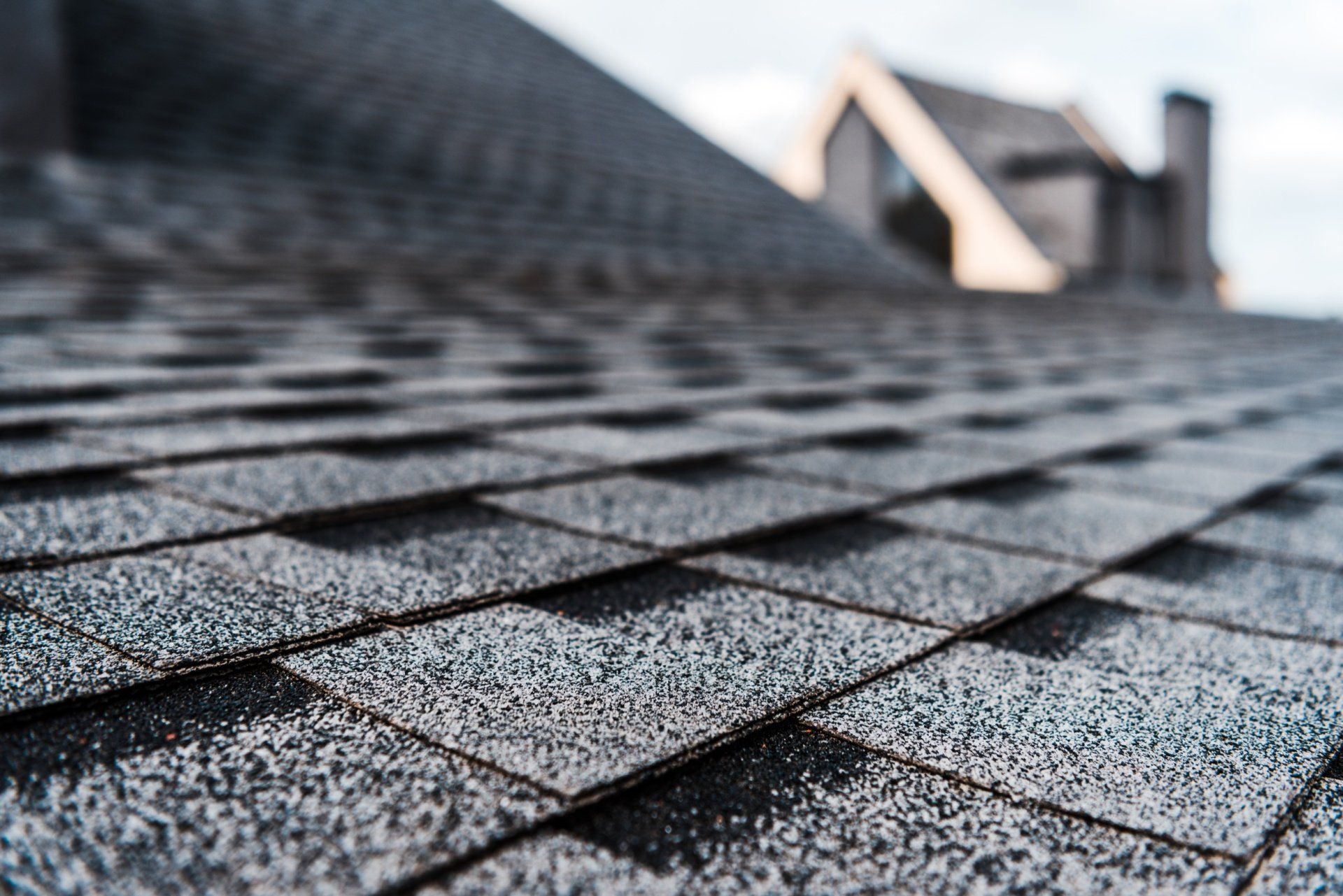 Close-up of gray roof shingles with a blurred rooftop vent in the background