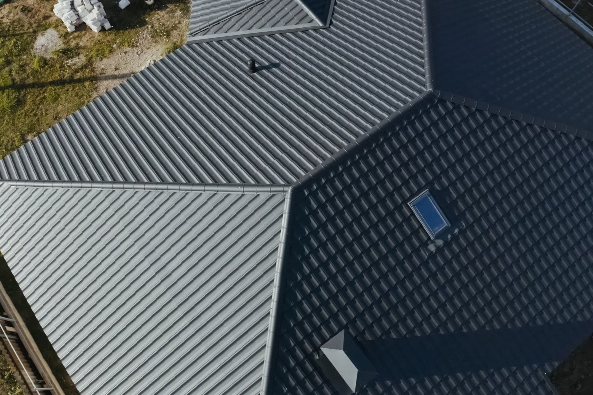 Aerial view of a house roof with gray and dark metal panels and a skylight