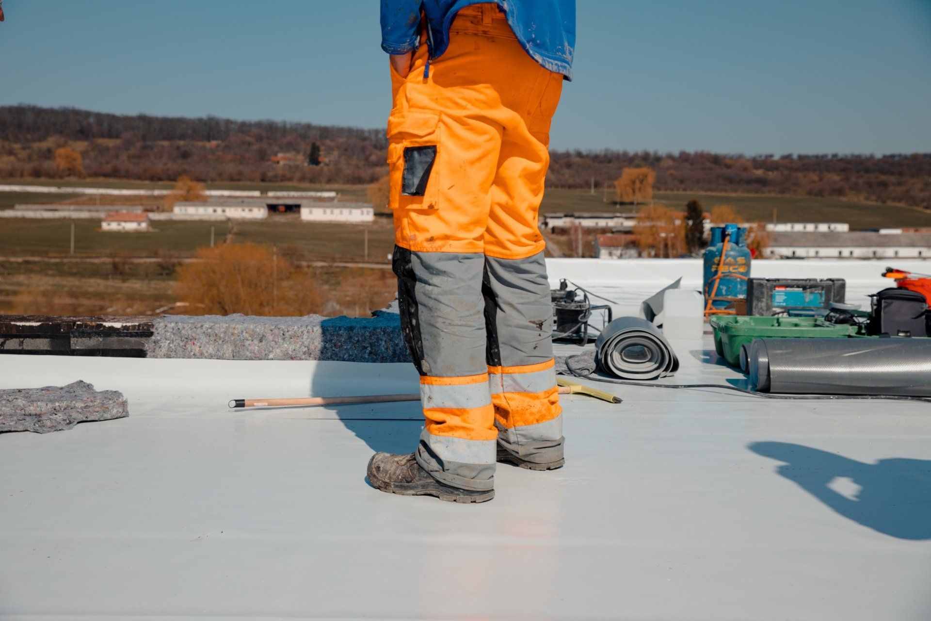 Worker in orange safety pants standing on a flat rooftop with construction materials nearby.
