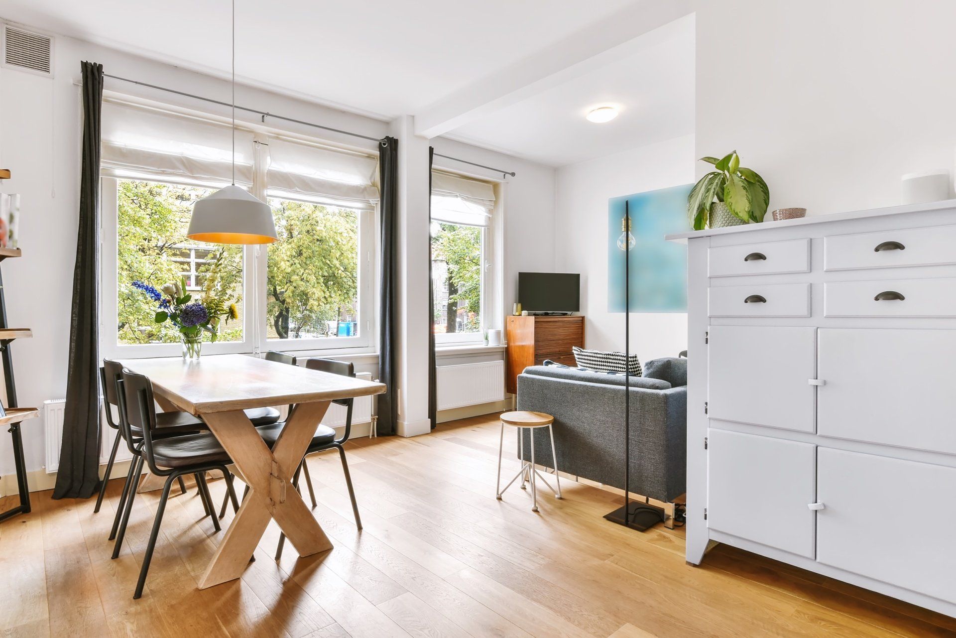 Bright dining room with large windows, wooden table, black chairs, couch, and white storage cabinet.