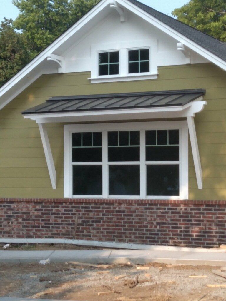 Small house exterior with olive siding, white trim, brick base, and front windows under a steep roof