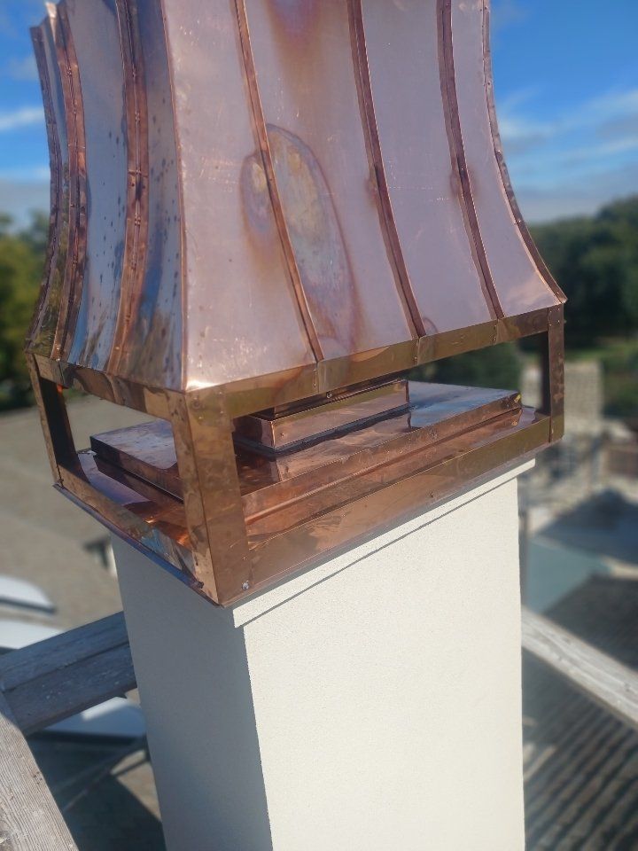 Close-up of a copper rooftop vent on a white chimney against a blue sky.