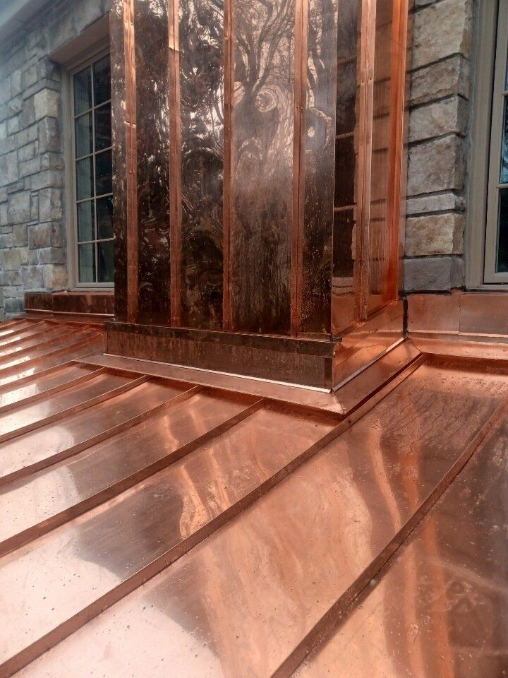 Copper-clad entrance with reflective metal panels and steps beside a stone building