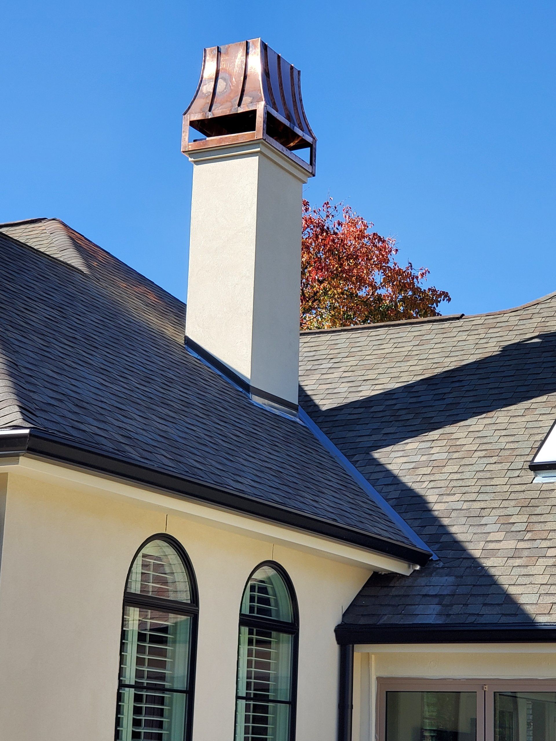 House roof with a tall chimney against a blue sky, with red autumn leaves in the background