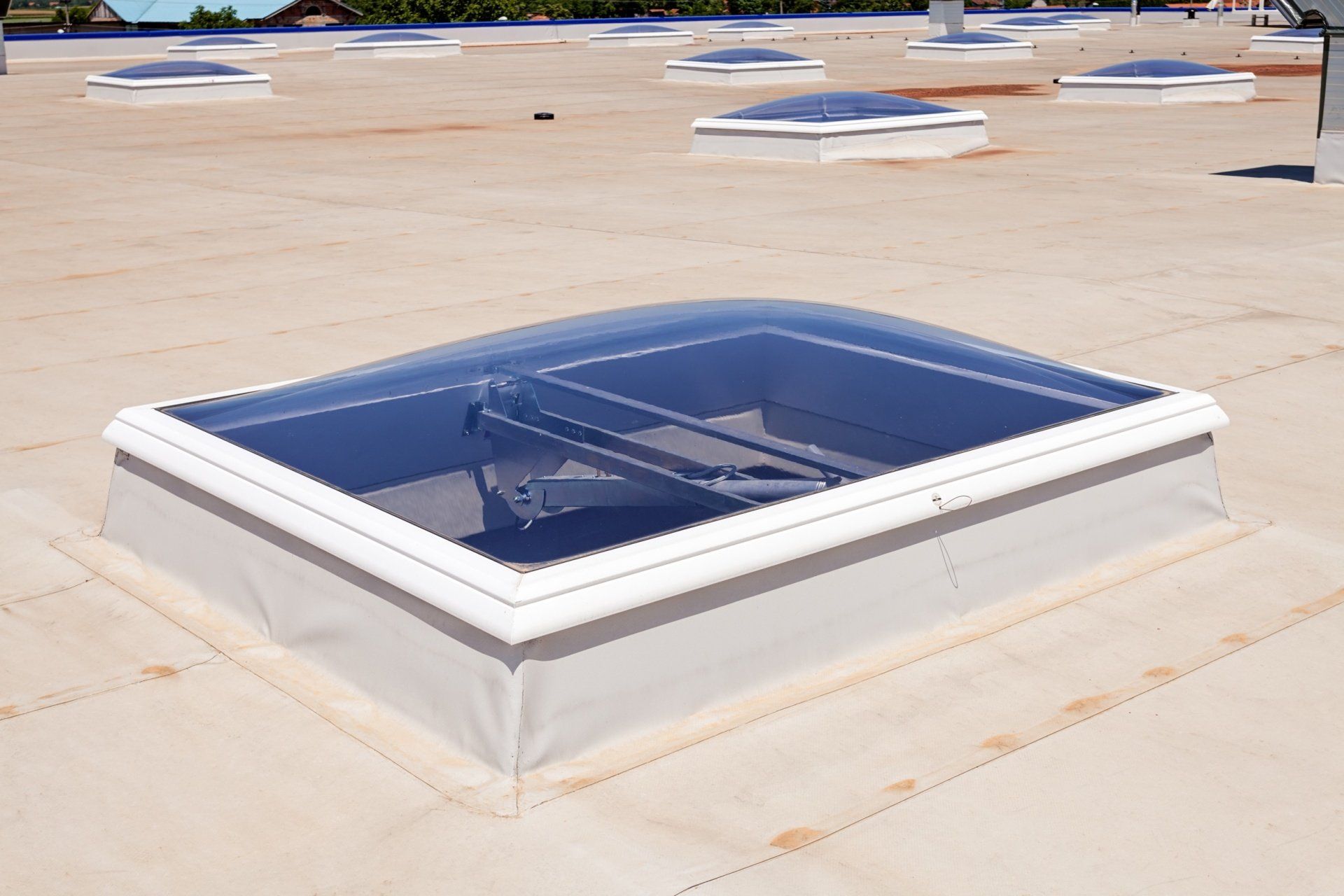 Rooftop skylight with dark blue glass on a flat beige roof under clear daylight