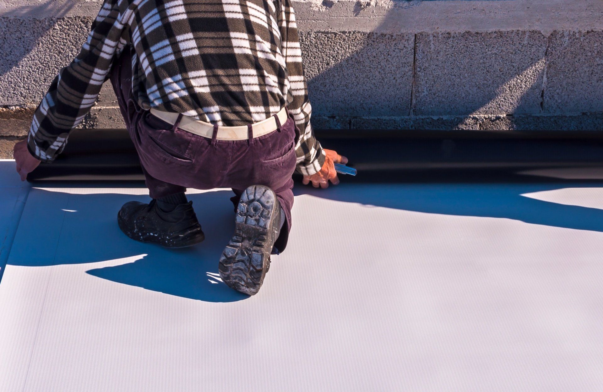 Person kneeling on a rooftop, working on a white surface with tools near a blue edge.