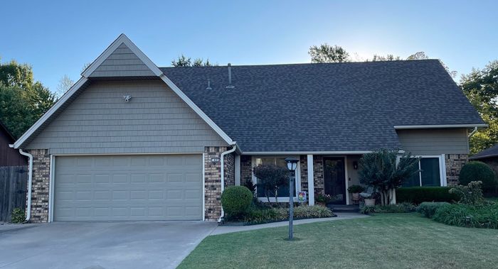 Suburban house with attached garage, dark roof, front lawn, and covered porch in daylight
