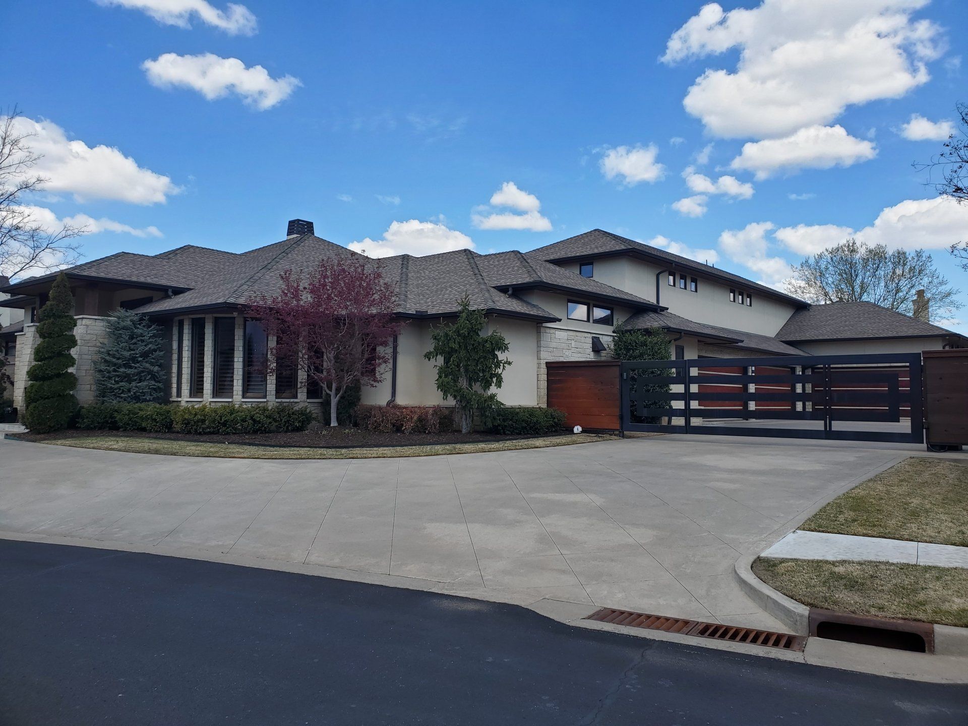 Suburban house with a gated driveway, garage, and blue sky with clouds