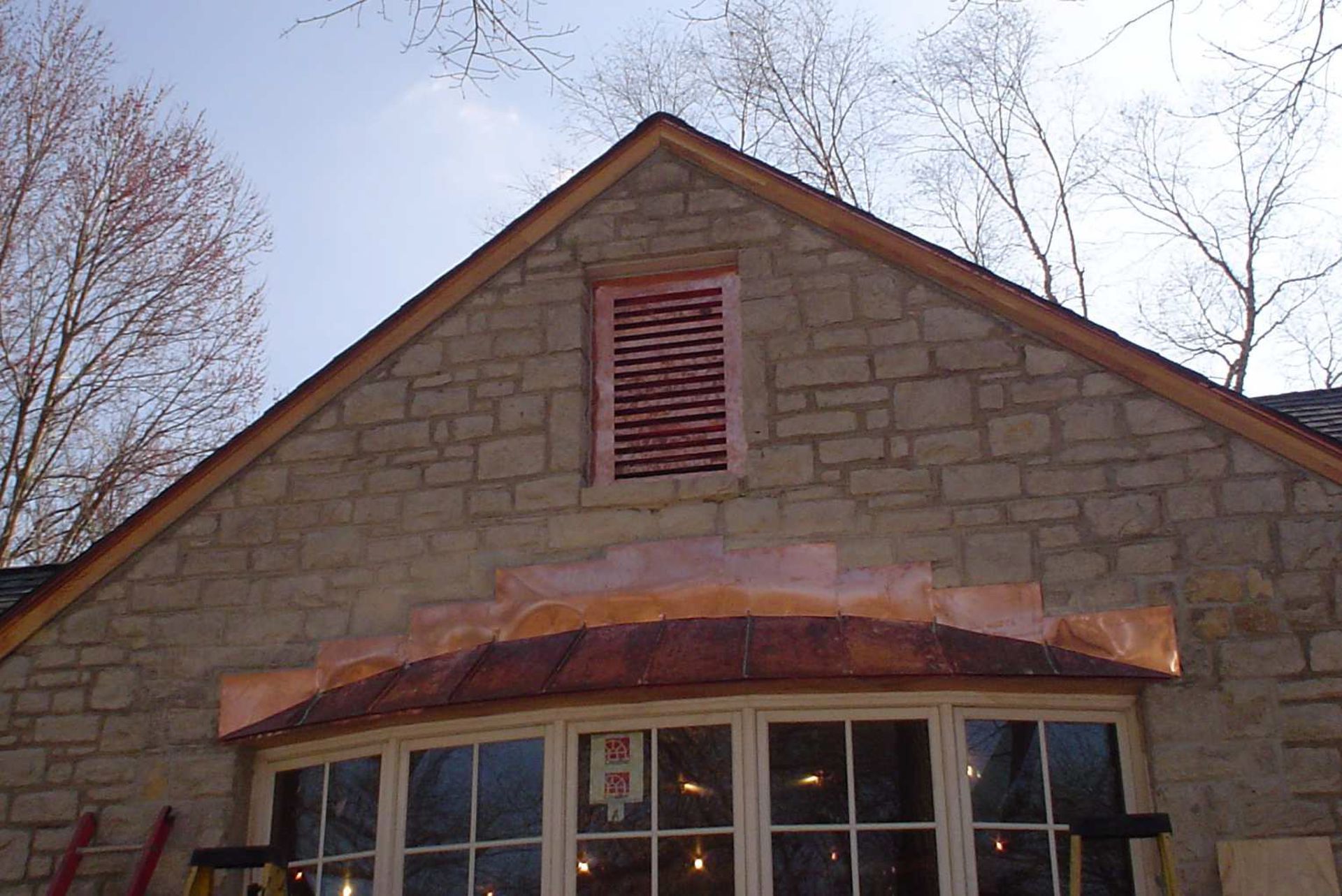 Stone building facade with red vent and arched window under a peaked roof