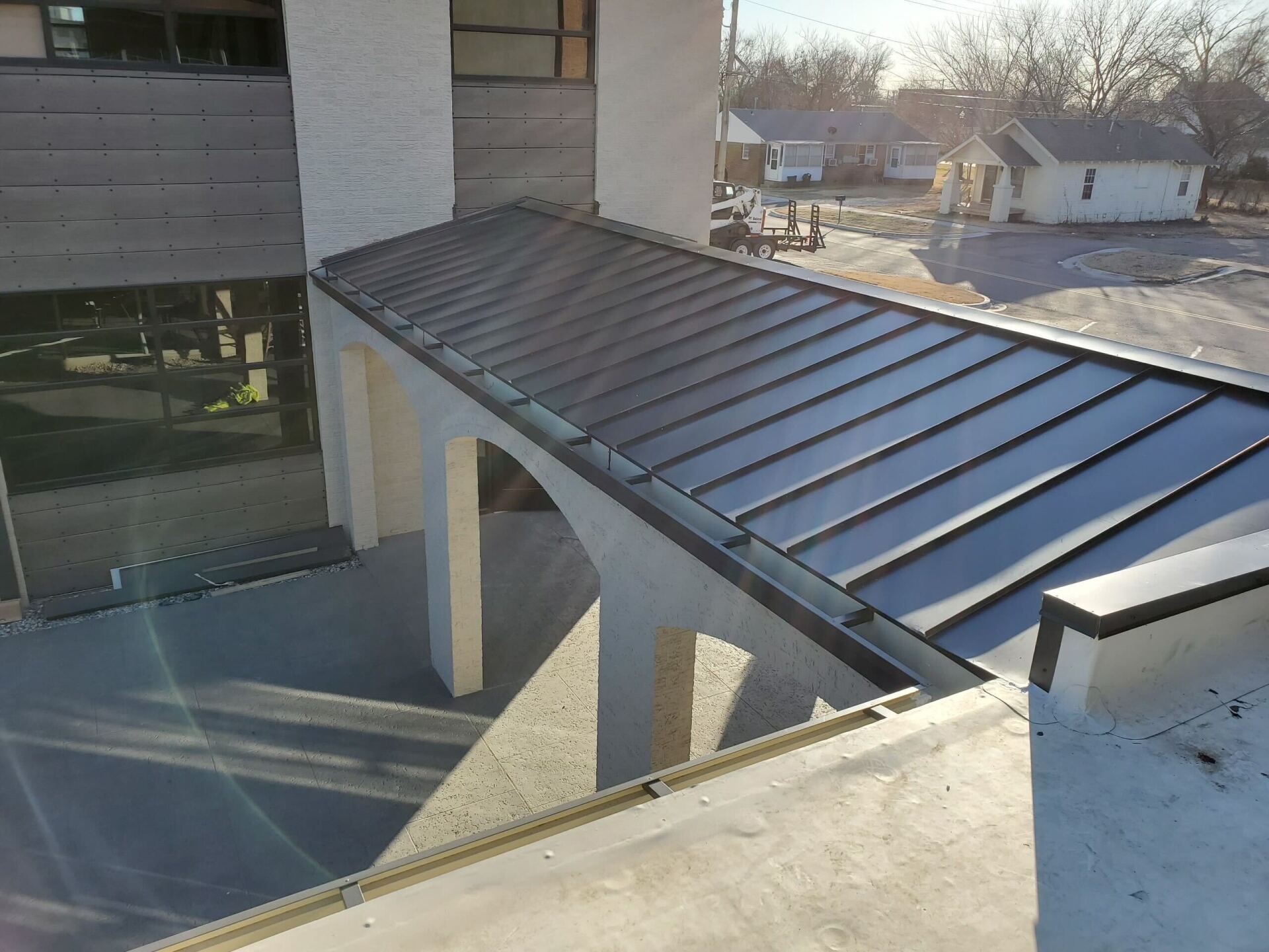 Rooftop walkway with a black metal roof beside a building, overlooking a residential area