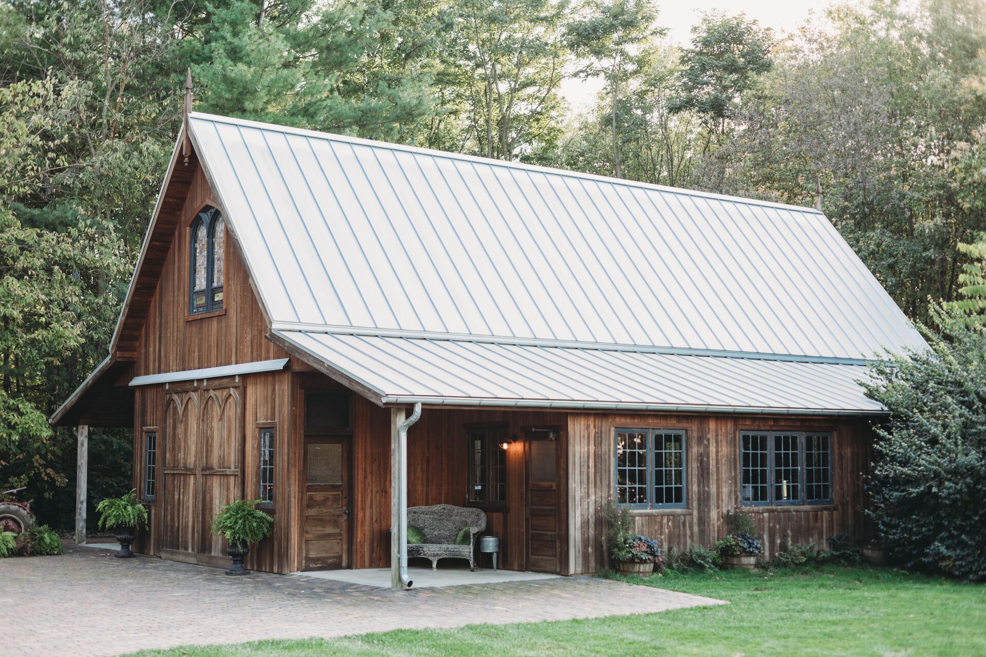 Rustic wooden cabin with a metal roof, porch, and green yard surrounded by trees