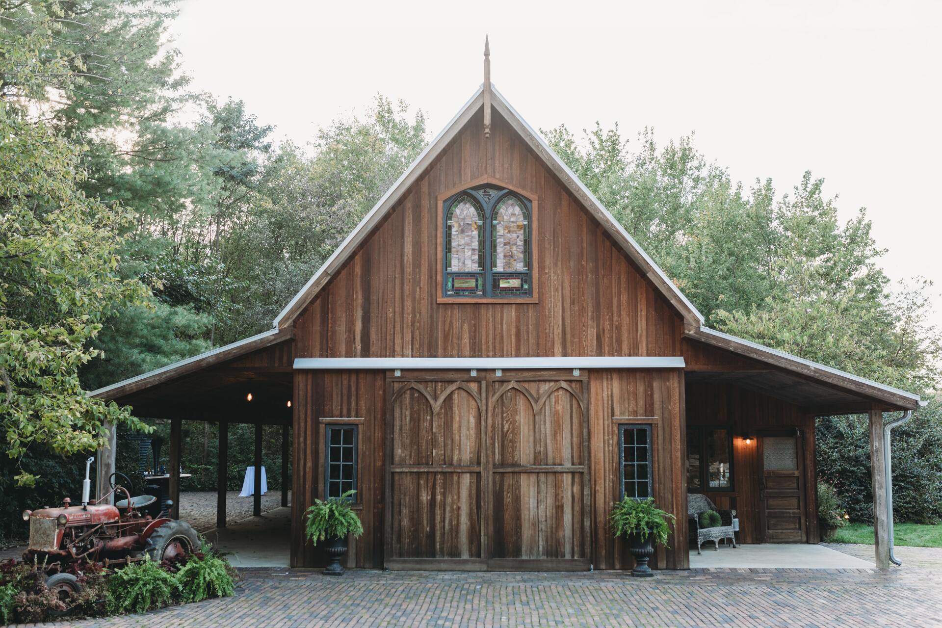 Rustic wooden chapel with steeple and arched windows, surrounded by trees and gravel driveway