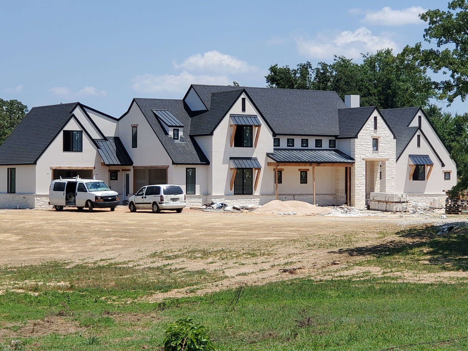 Large modern house under construction with gray roof and white exterior, two vehicles parked in front.